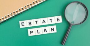 Estate Plan spelled with scrabble tiles on green background with notebook and magnifying glass.